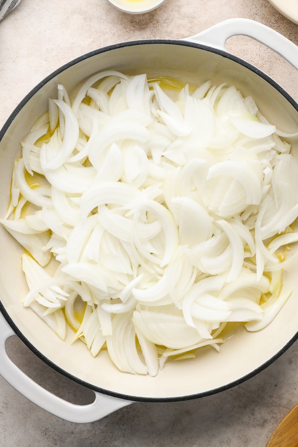 Sliced white onions cooking in oil in a white enameled cast iron pot.