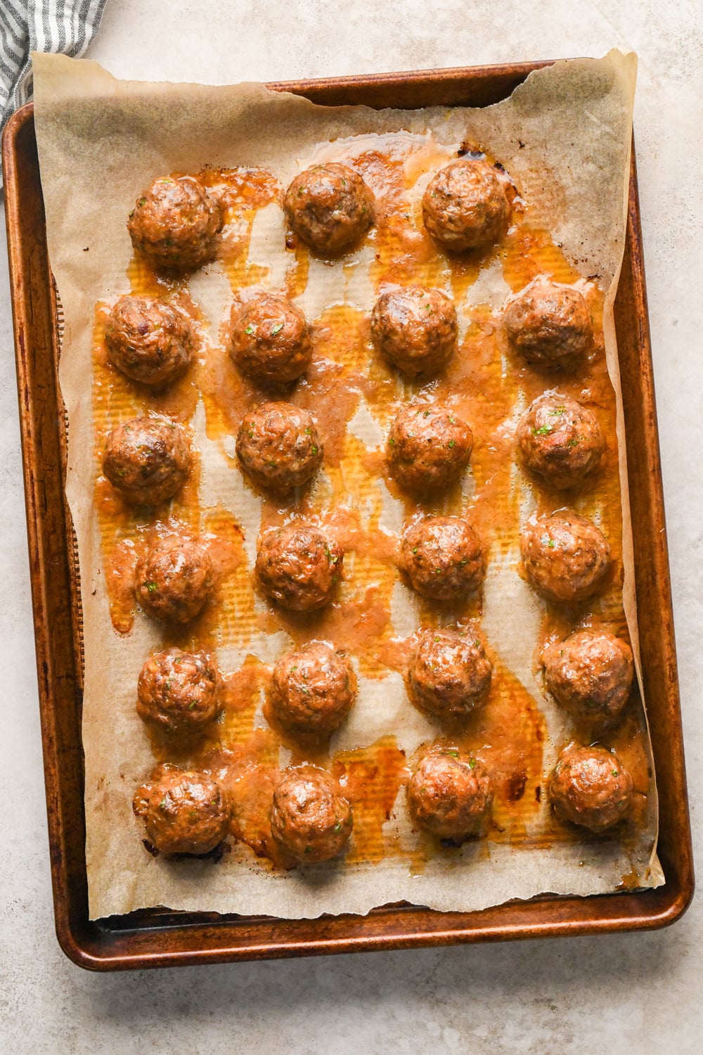 A baking sheet lined with parchment paper holds twenty-three cooked meatballs.