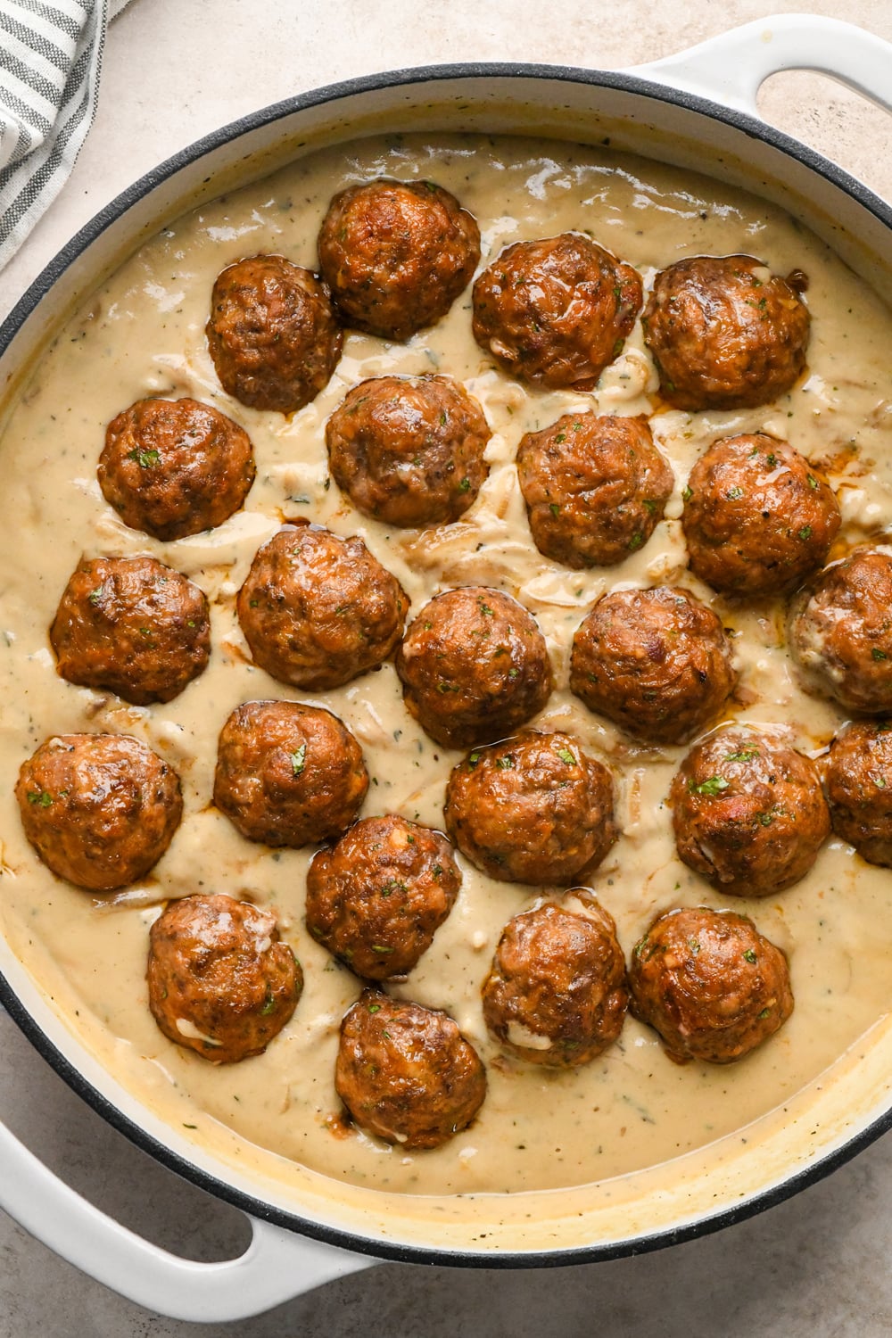 Meatballs added to the creamy caramelized onion gravy in a wide white skillet.