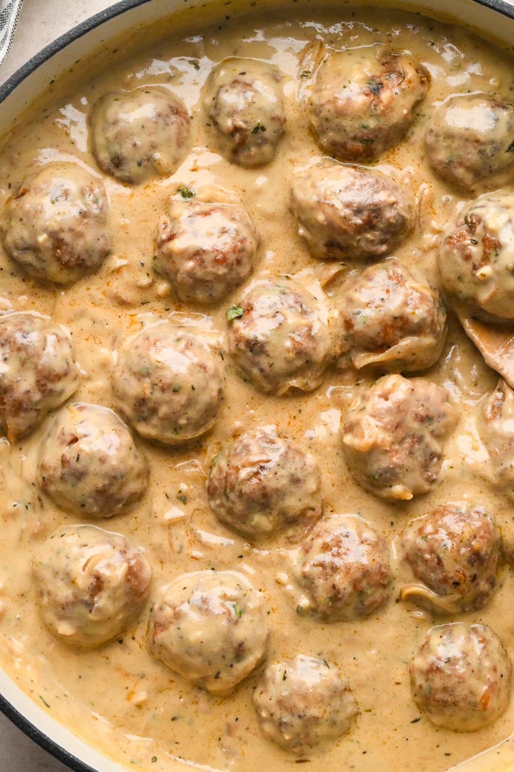 Meatballs covered with the creamy caramelized onion gravy in a wide white skillet.