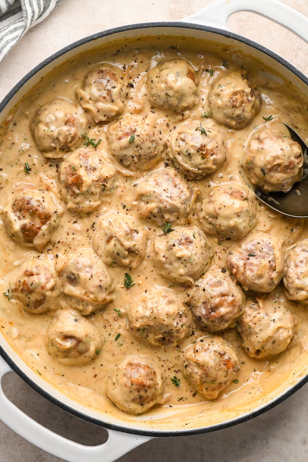 Meatballs covered with the creamy caramelized onion gravy in a wide white skillet, garnished with fresh thyme and black pepper.