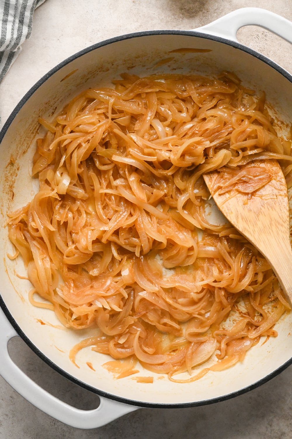 Deeply caramelized sliced white onions in a white cast iron skillet.